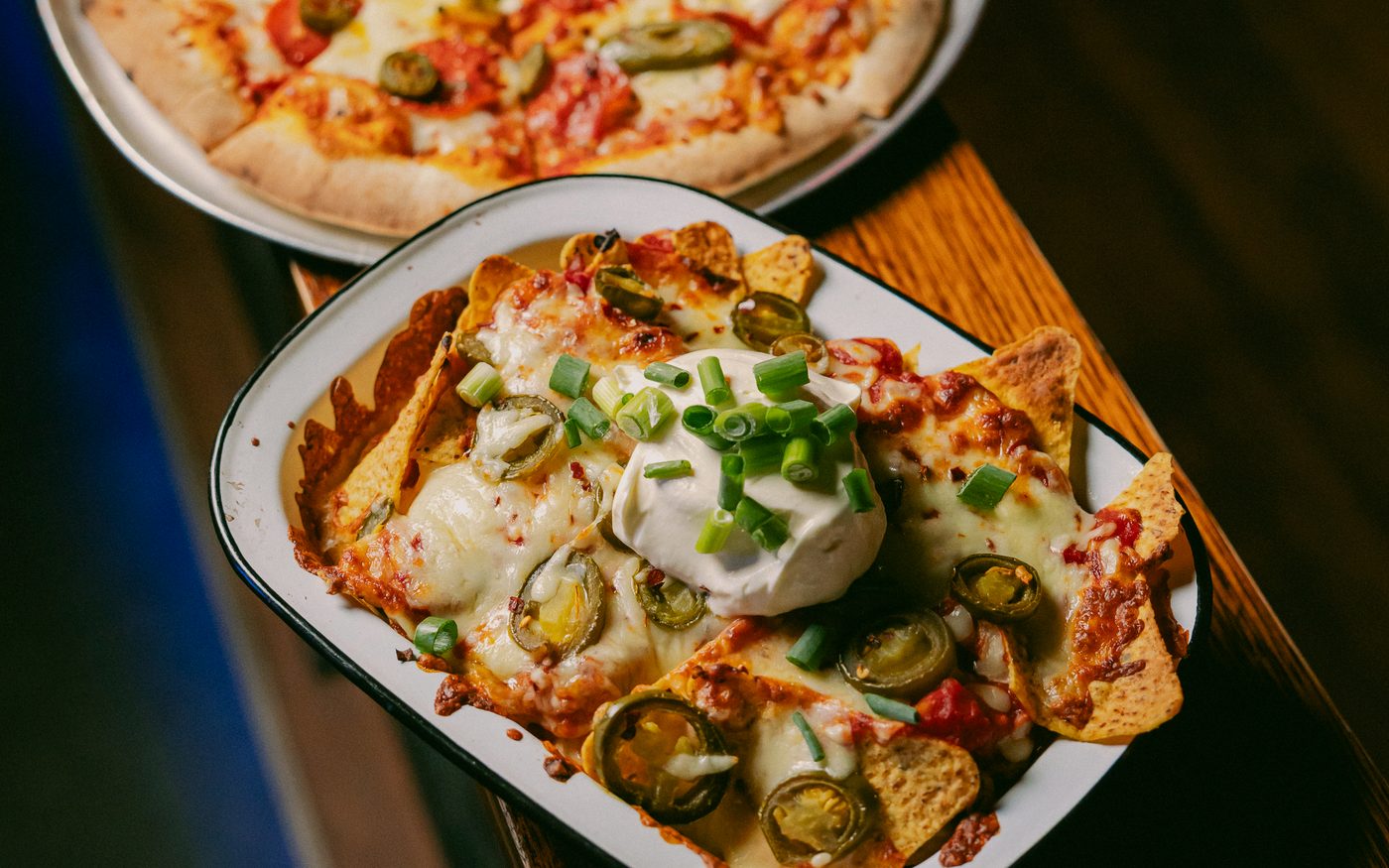Loaded jalapeño nachos with sour cream and spring onion beside a jalapeño pizza