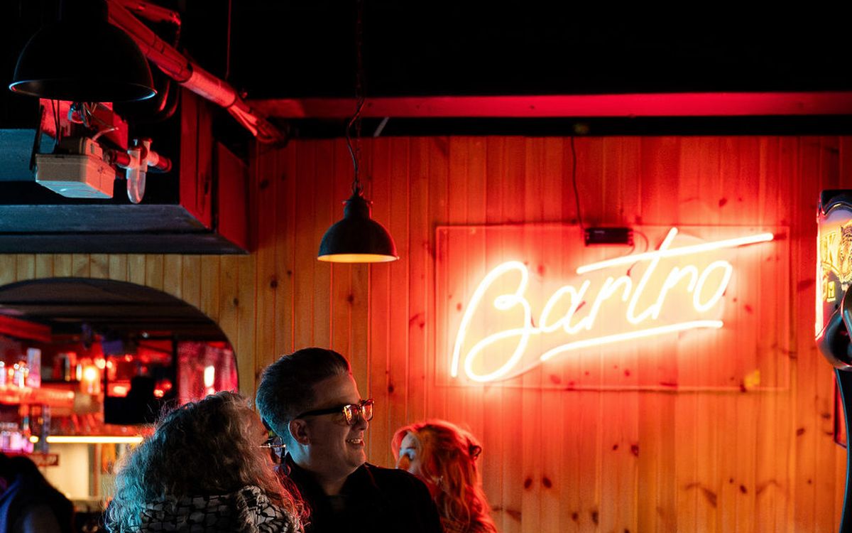 Guests playing a light-gun cabinet under the red Bartronica neon